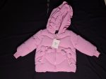 Front view of a girls' pink polyester jacket with a ruffled hood and butterfly details, laid flat on a black surface.