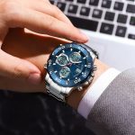 A man wearing the POEDAGAR E102 digital watch with a silver stainless steel band and a blue dual-display dial.