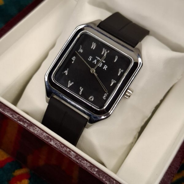 A SABR 1037B model watch with a silver square case and black dial with Arabic numerals, shown resting in its white display box.