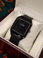 A black square-faced SABR 1037B watch with a black strap, shown from an angle inside its presentation box.