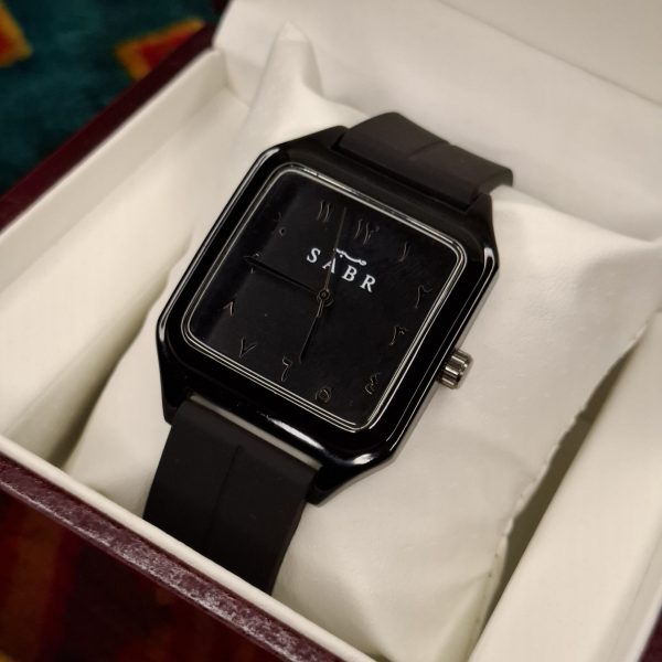 A black square-faced SABR 1037B watch with a black strap, shown from an angle inside its presentation box.