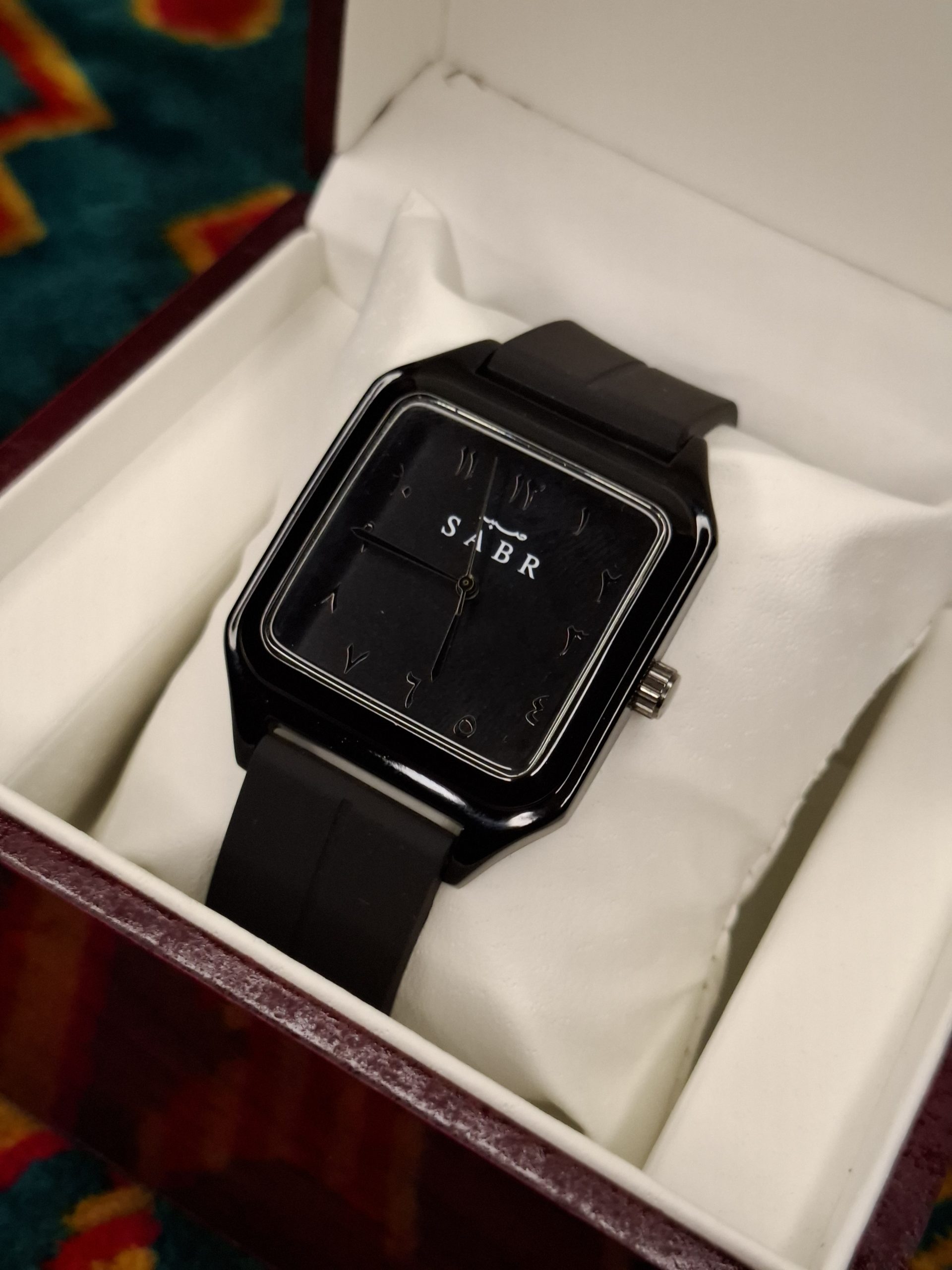 A black square-faced SABR 1037B watch with a black strap, shown from an angle inside its presentation box.