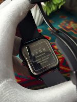 A person wearing a white glove holds up the SABR 1037B watch to show the engraved stainless steel case back.