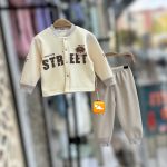 A baby's cream and grey thermal set with a button-up jacket and pants hanging on a hanger. The jacket has a 'STREET' print.