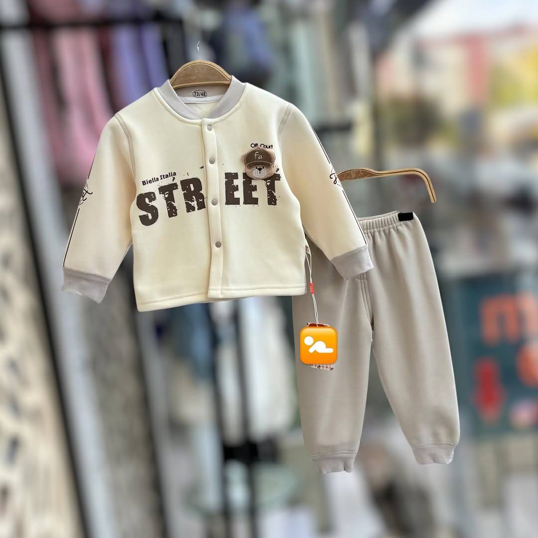A baby's cream and grey thermal set with a button-up jacket and pants hanging on a hanger. The jacket has a 'STREET' print.