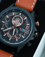 A CURREN 8380 chronograph men's watch with a brown leather strap and rose gold details, displayed on a dark textured surface.