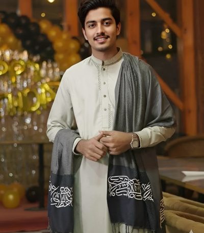 A man wearing a light tunic with a dark grey Arabic Calligraphy Shawl draped over his shoulder.