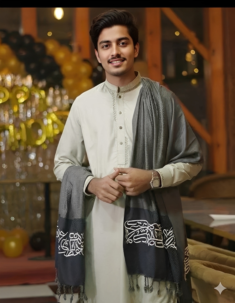 A man wearing a light tunic with a dark grey Arabic Calligraphy Shawl draped over his shoulder.