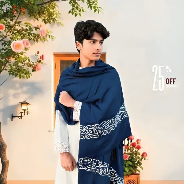 A young man models a large blue Arabic calligraphy shawl with white script-like patterns and blue tassels over a white outfit.
