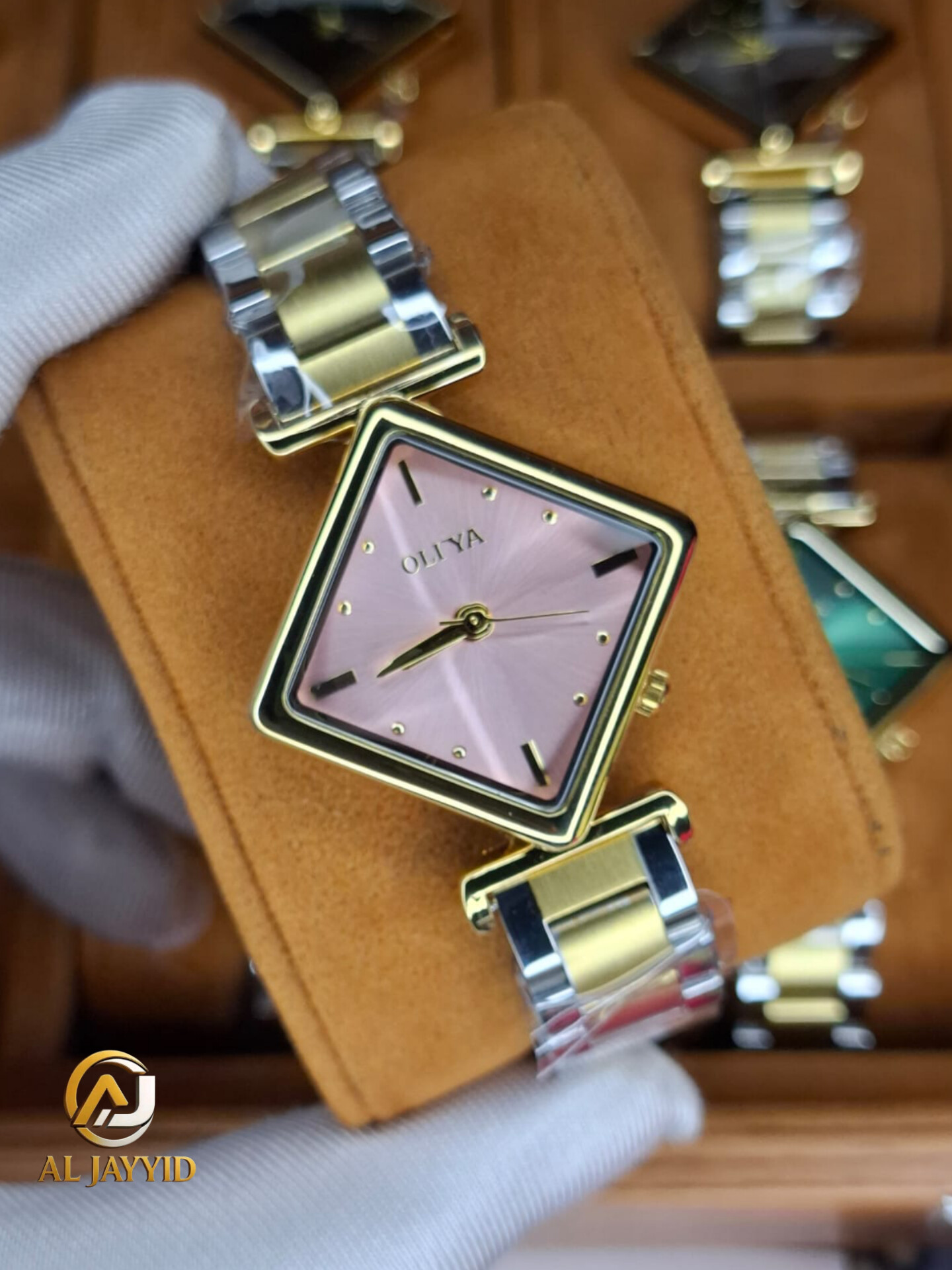 A gloved hand holding the OLIYA 6819 women's two-tone watch, showing its pink square dial and gold and silver-tone bracelet.