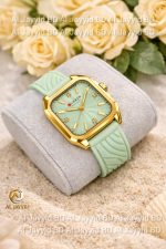 A Curren 9113 women's watch with a green square dial and silicone strap, resting on a cushion with flowers behind it.