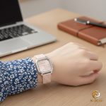 A woman wearing the Curren 9113 square silicone watch with a pink dial and strap, resting her hand on a wooden desk.