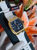 A CURREN 8488 Men's Square Chronograph Watch with a gold case, blue dial, and white strap, displayed on a flower background.