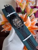 A gloved hand holds a CURREN 8488 men's watch with a black square case, rose gold details, and a black silicone strap.