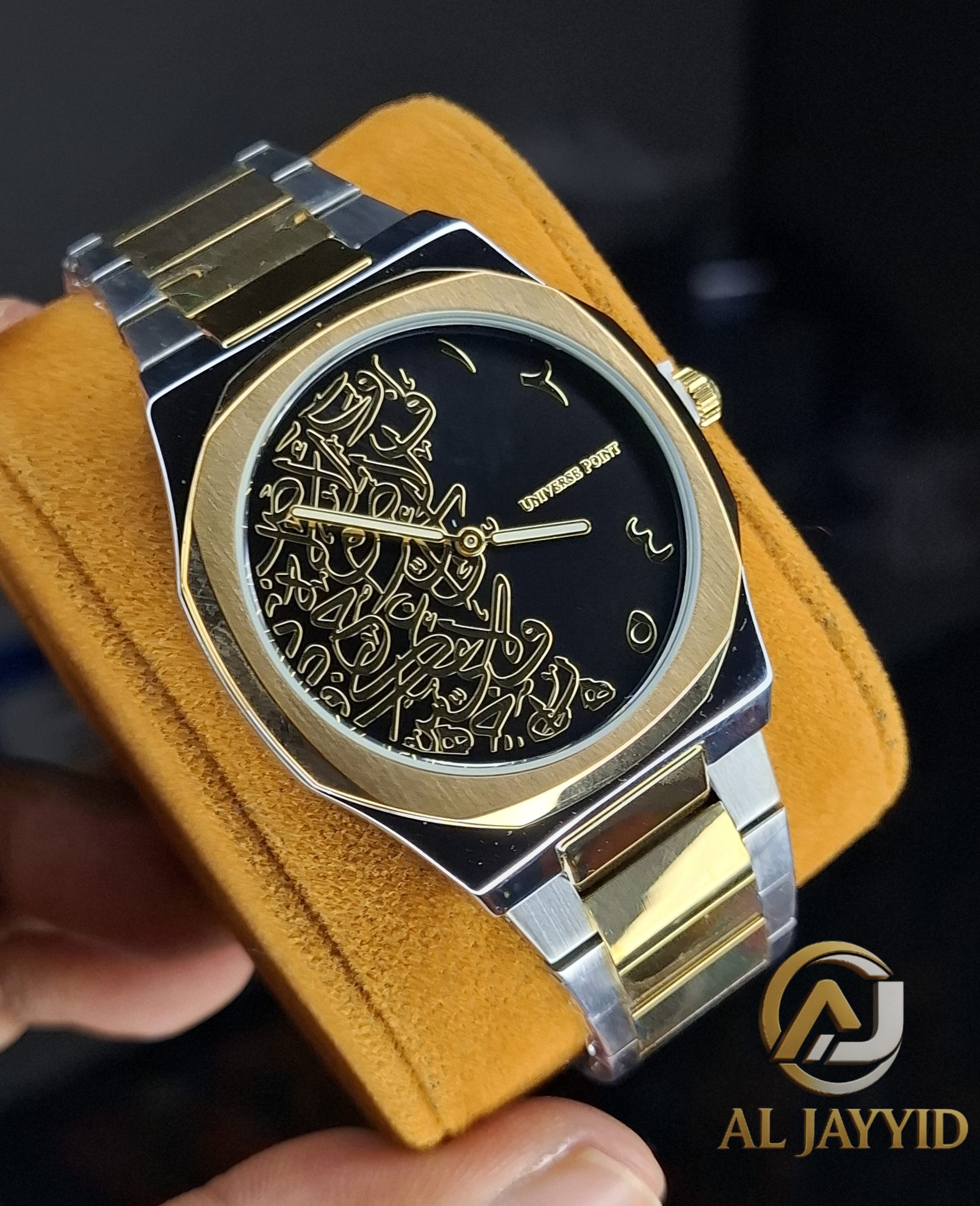 Universe Point Arabic Calligraphy Watch A Universe Point Arabic Calligraphy Watch with a two-tone gold and silver band, held on a yellow cushion to show the black dial.