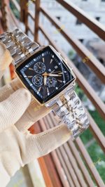 A hand in a beige glove holding a POEDAGAR 866 luxury square wristwatch with a black dial and two-tone bracelet.