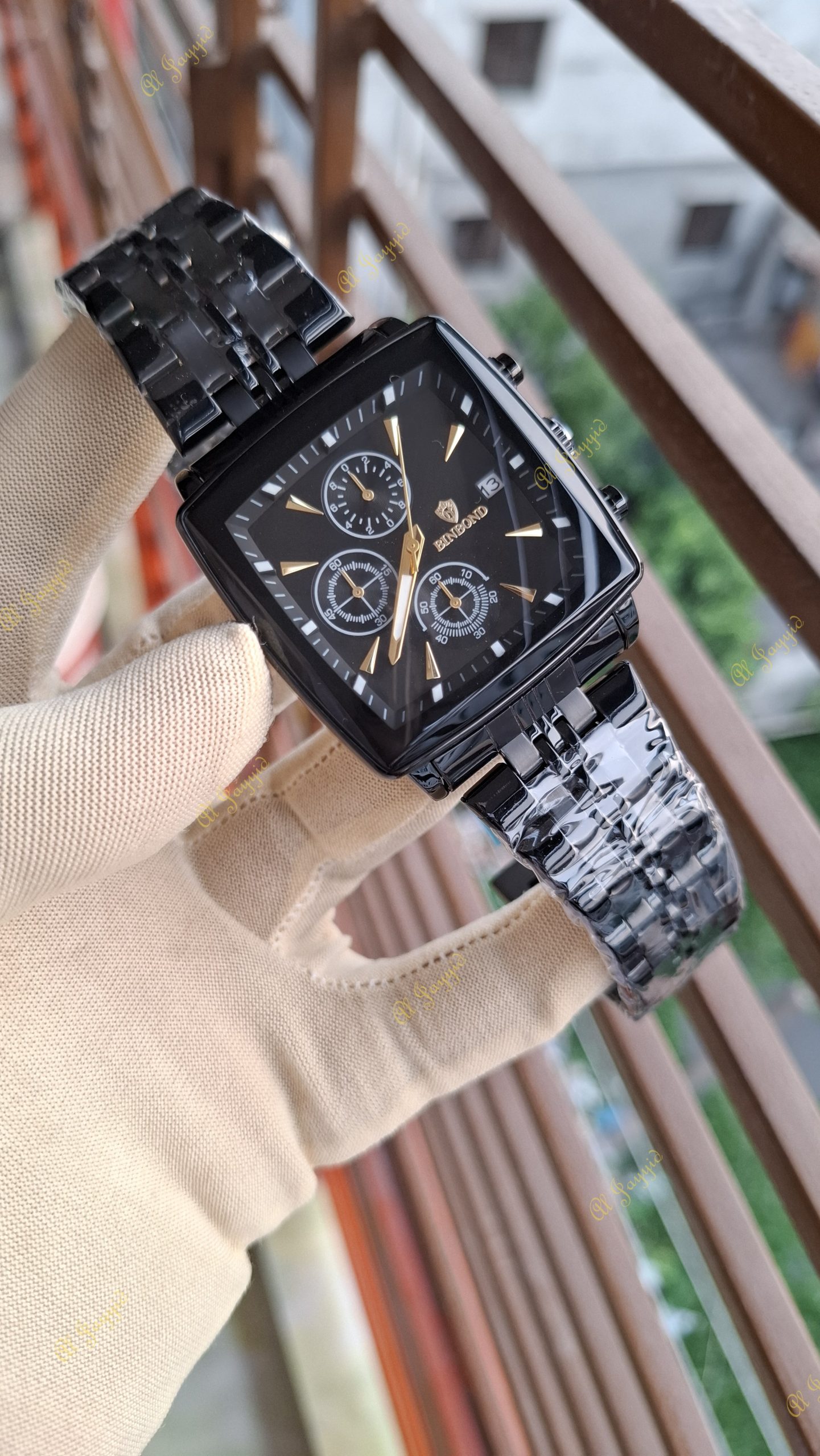 A hand in a beige glove holds up a Binbond 911 Original Men’s Luxury Watch with a square black case and gold accents.
