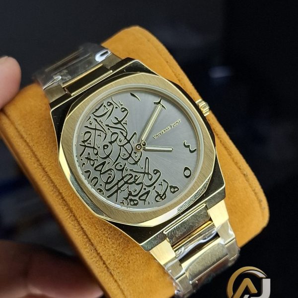 A gold-colored Universe Point watch with a metal bracelet, featuring a grey dial with intricate black Arabic calligraphy.