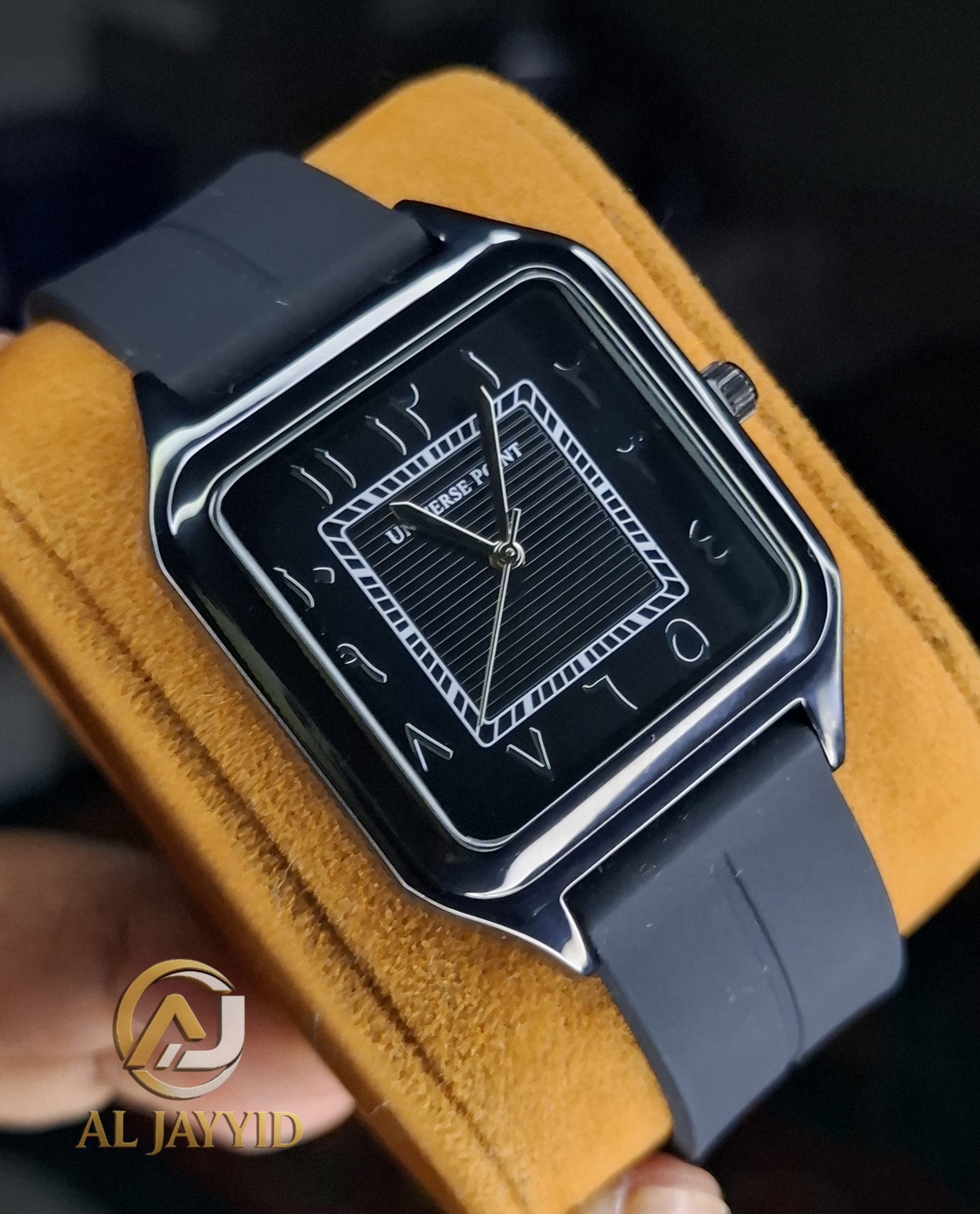 A Universe Point black silicone watch with a square face and Arabic numerals, shown at an angle on a yellow surface.