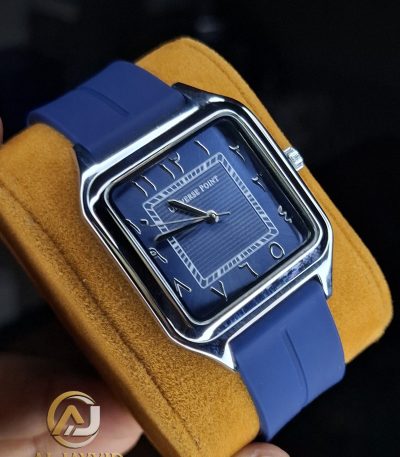 A Universe Point watch with a square, blue dial, Arabic numerals, and a matching blue silicone strap, held on a yellow cushion.