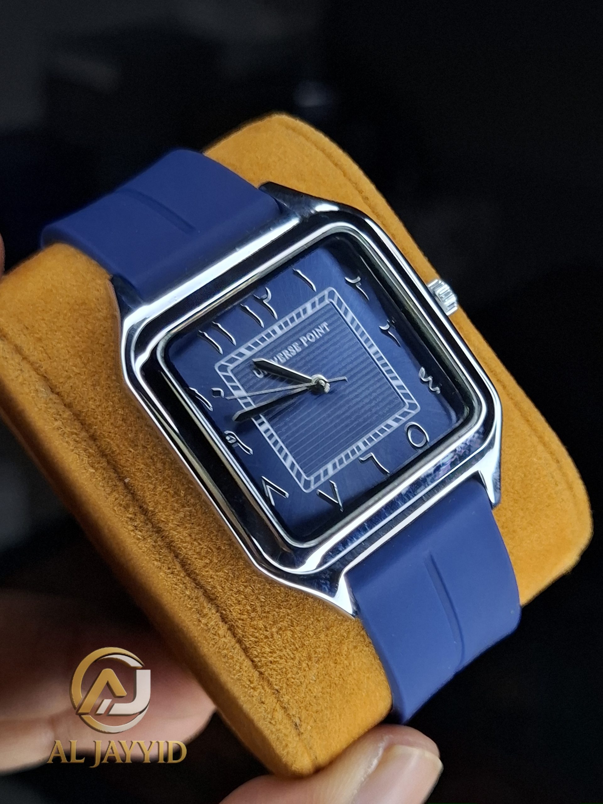 Universe Point Watch with Arabic Numerals and Silicone Strap A Universe Point watch with a square, blue dial, Arabic numerals, and a matching blue silicone strap, held on a yellow cushion.