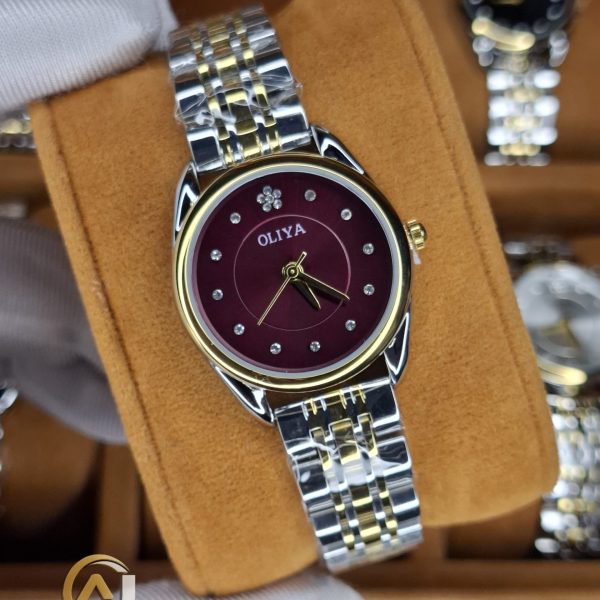 A gloved hand holding the OLIYA 6658 women's watch, showcasing its two-tone silver and gold band and deep red dial.