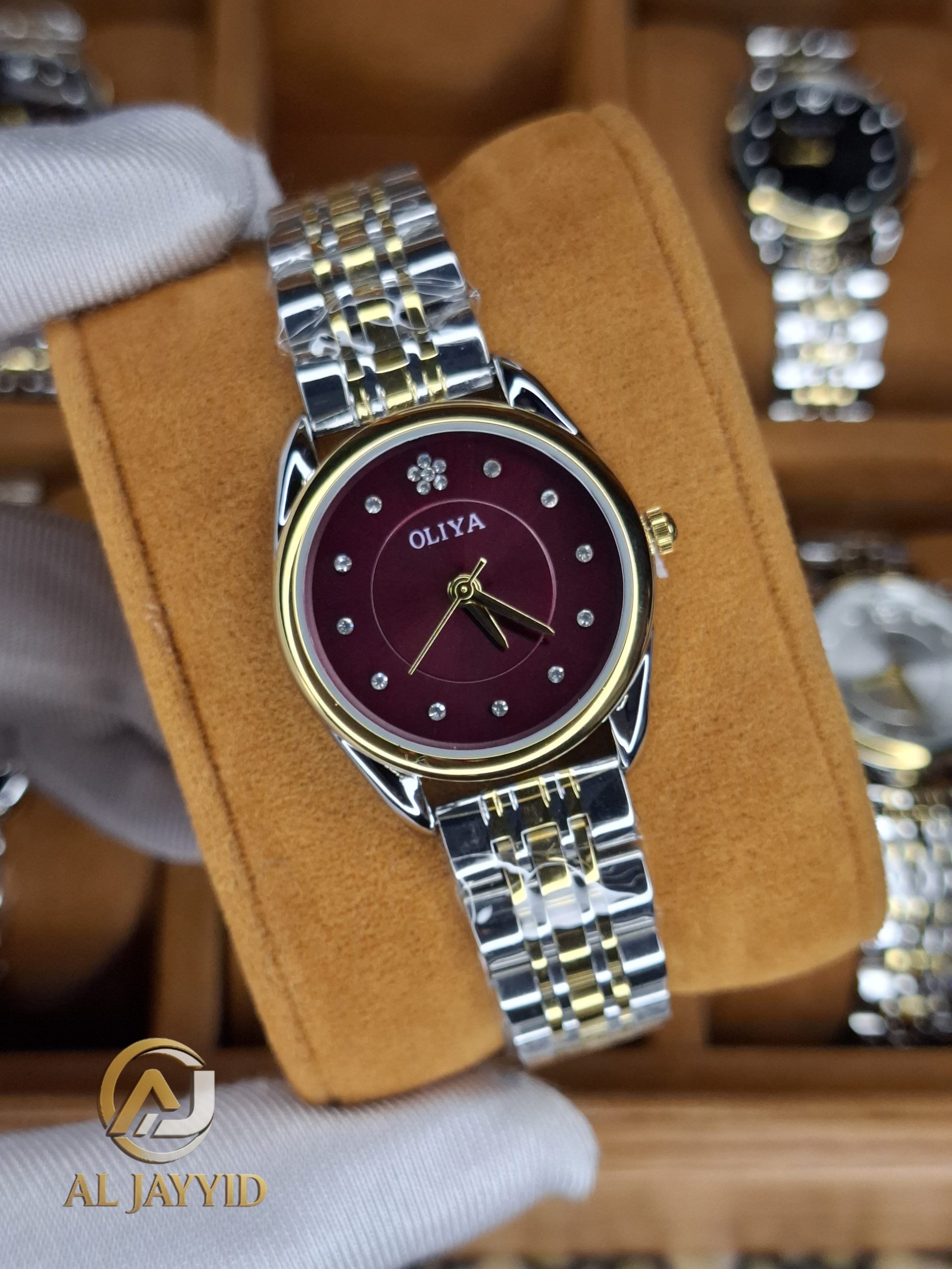 A gloved hand holding the OLIYA 6658 women's watch, showcasing its two-tone silver and gold band and deep red dial.