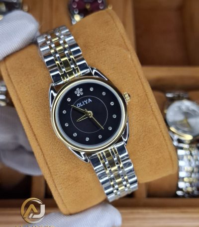 A gloved hand holding the OLIYA 6658 women's watch, which has a two-tone gold and silver strap and a black dial.