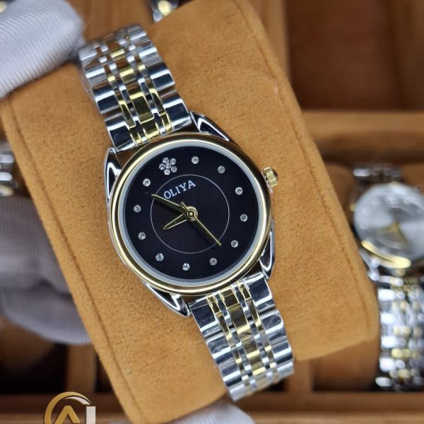 A gloved hand holding the OLIYA 6658 women's watch, which has a two-tone gold and silver strap and a black dial.