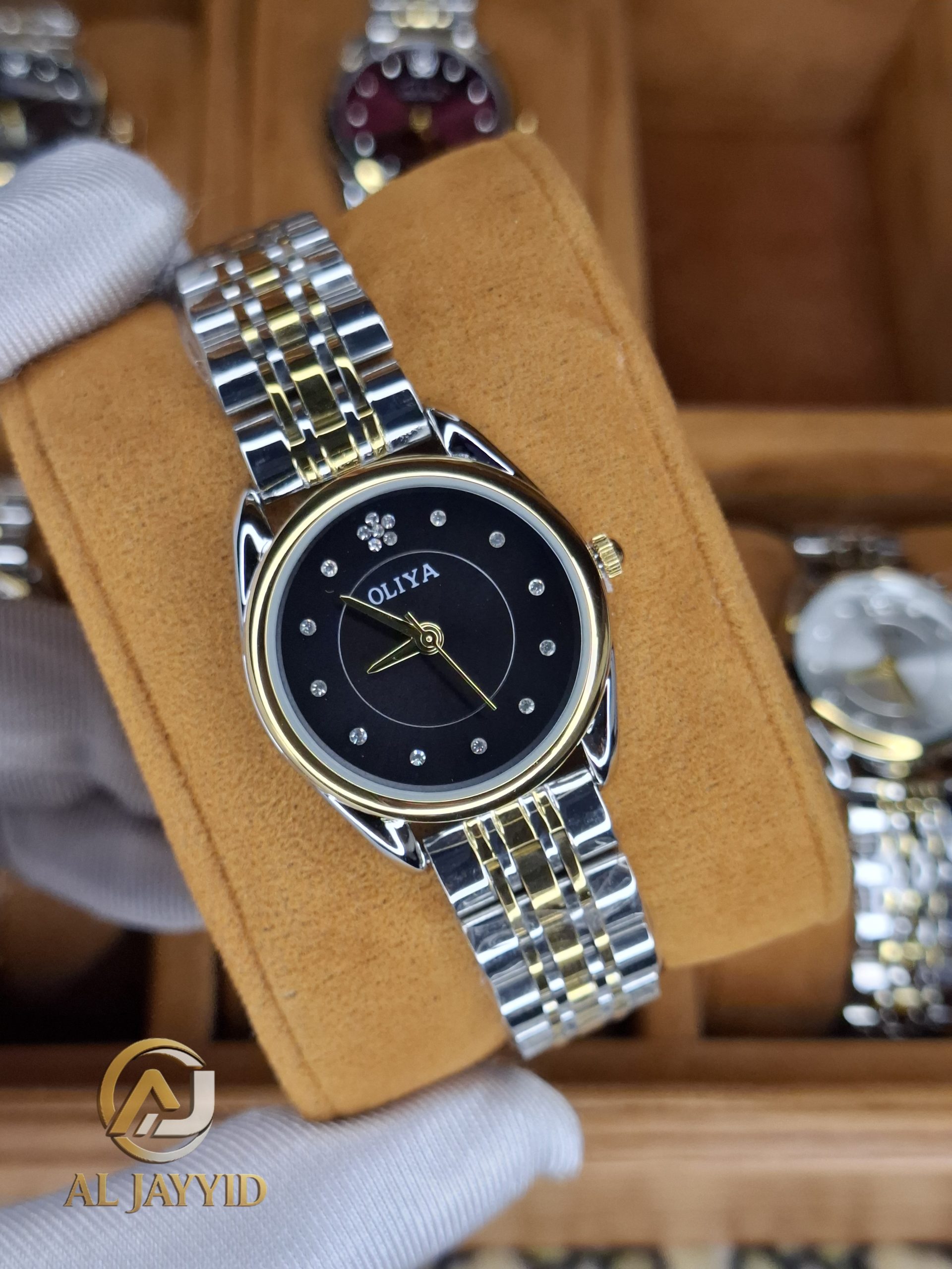 A gloved hand holding the OLIYA 6658 women's watch, which has a two-tone gold and silver strap and a black dial.