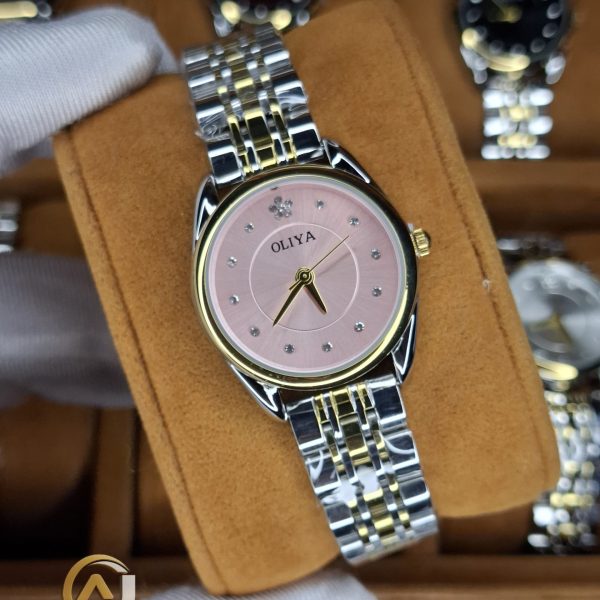 A gloved hand holding an OLIYA 6658 women's watch featuring a two-tone bracelet and a pink dial with crystal markers.
