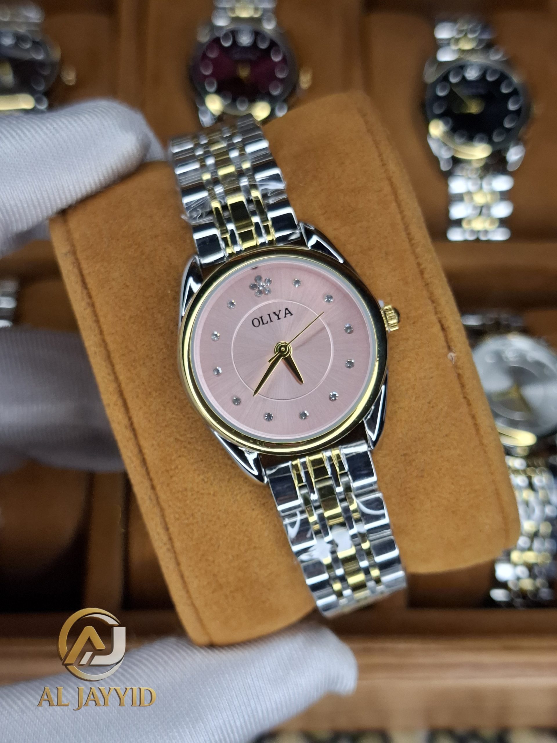 A gloved hand holding an OLIYA 6658 women's watch featuring a two-tone bracelet and a pink dial with crystal markers.