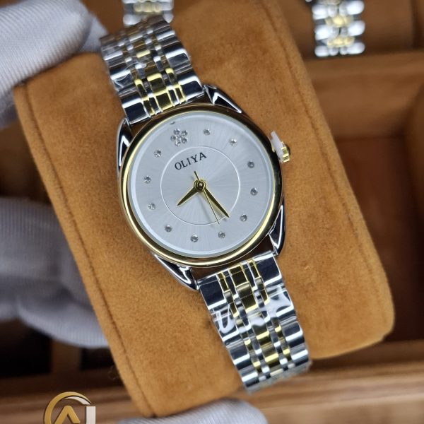 A gloved hand holding an OLIYA 6658 women's two-tone watch with a silver and gold band and a white crystal-studded dial.