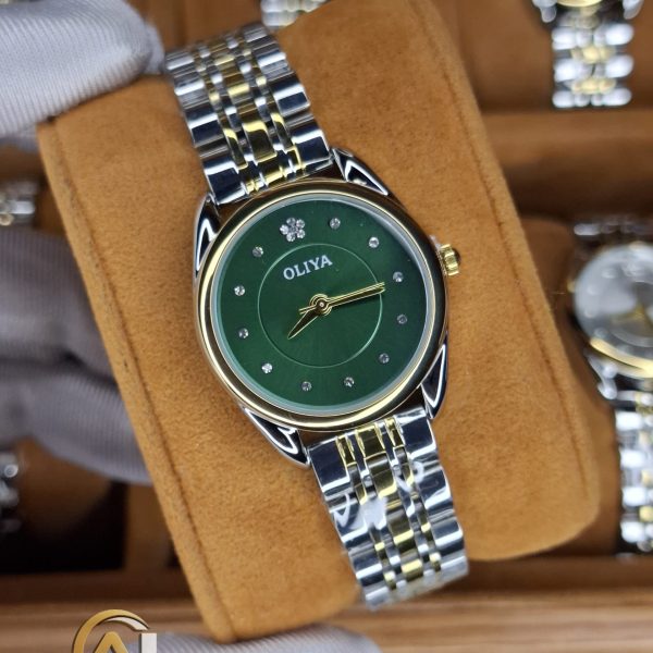 A gloved hand holding an OLIYA 6658 women's watch with a green dial and a two-tone silver and gold band.