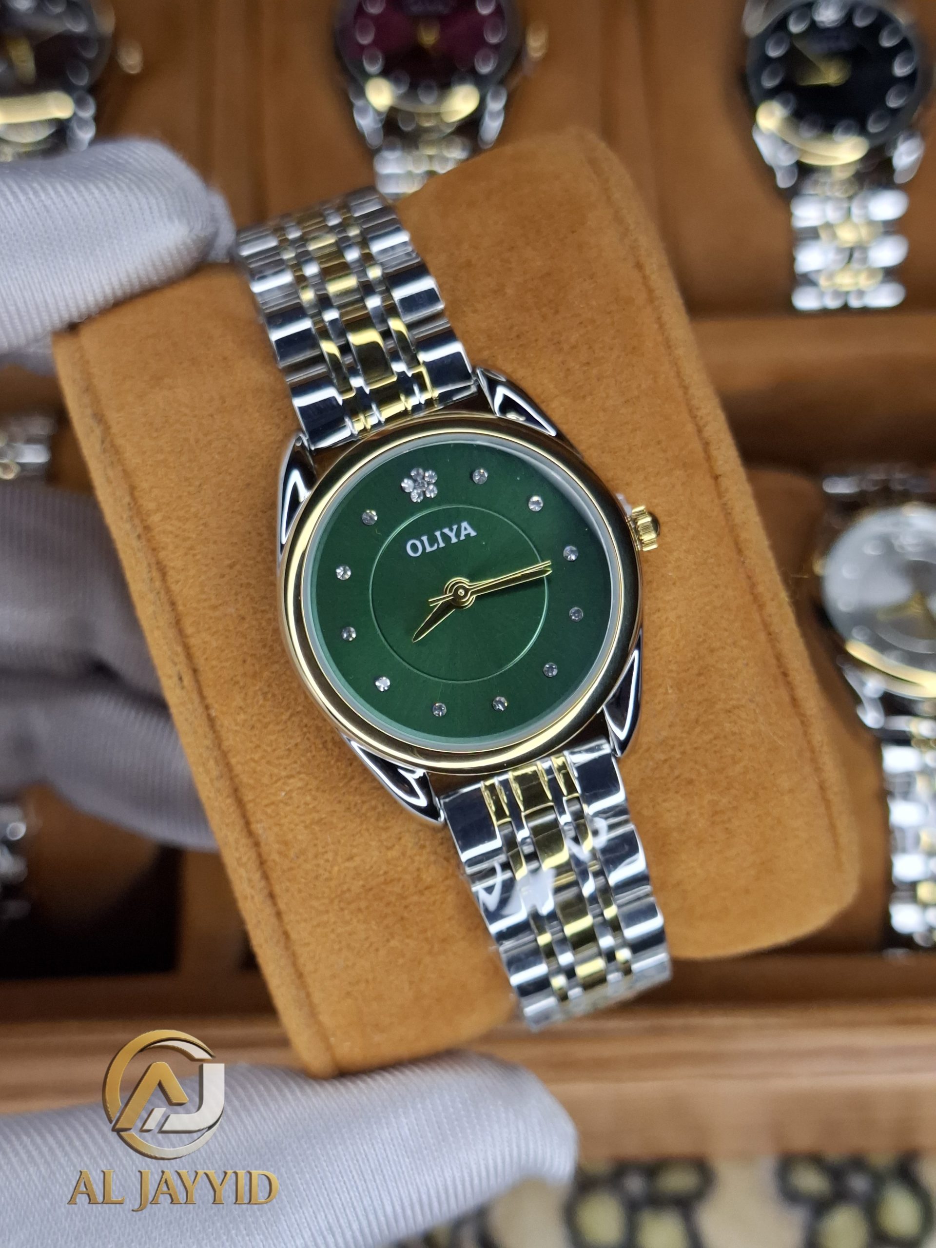 A gloved hand holding an OLIYA 6658 women's watch with a green dial and a two-tone silver and gold band.