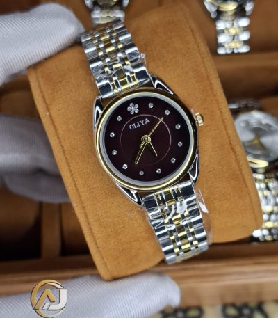 A gloved hand holding the OLIYA 6658 women's watch, showcasing its two-tone golden silver bracelet and coffee dial.