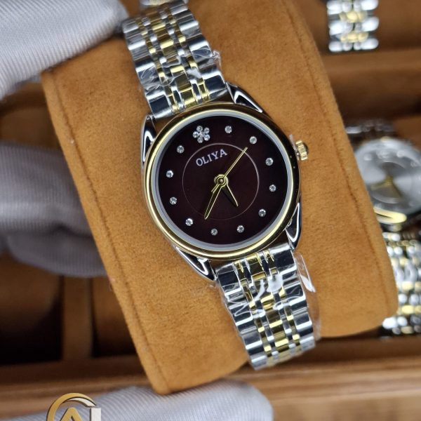 A gloved hand holding the OLIYA 6658 women's watch, showcasing its two-tone golden silver bracelet and coffee dial.