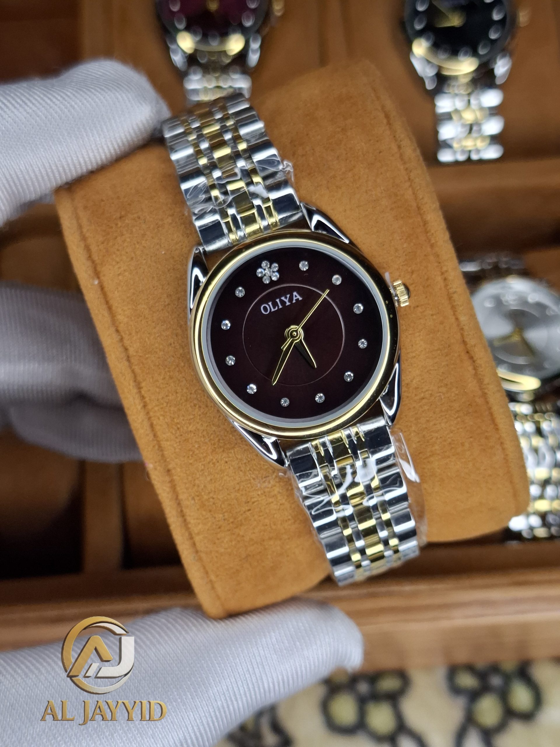 A gloved hand holding the OLIYA 6658 women's watch, showcasing its two-tone golden silver bracelet and coffee dial.