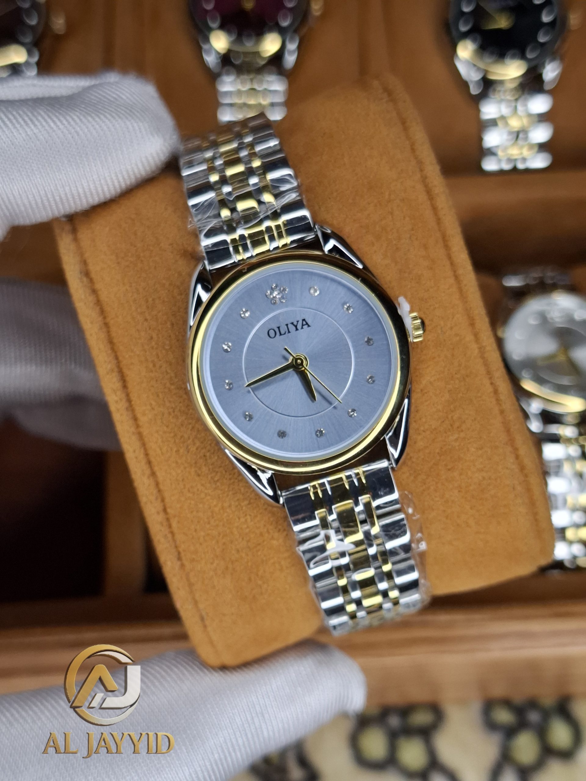 A gloved hand holding the OLIYA 6658 women's watch, which has a two-tone silver and gold band and a grey dial with crystals.