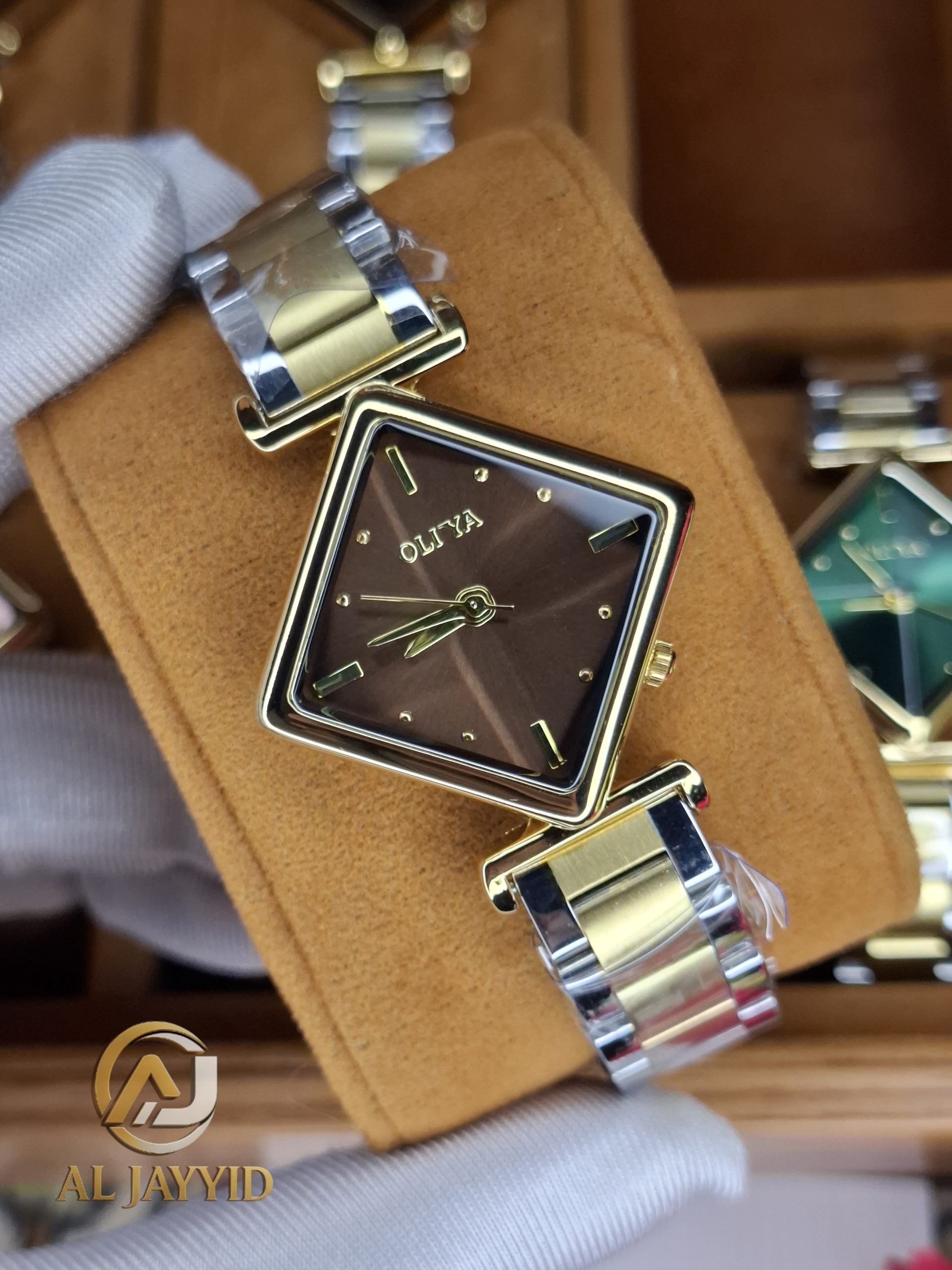A gloved hand holding the OLIYA 6819 Women's Two-Tone Watch, showing its square brown dial and gold and silver bracelet.
