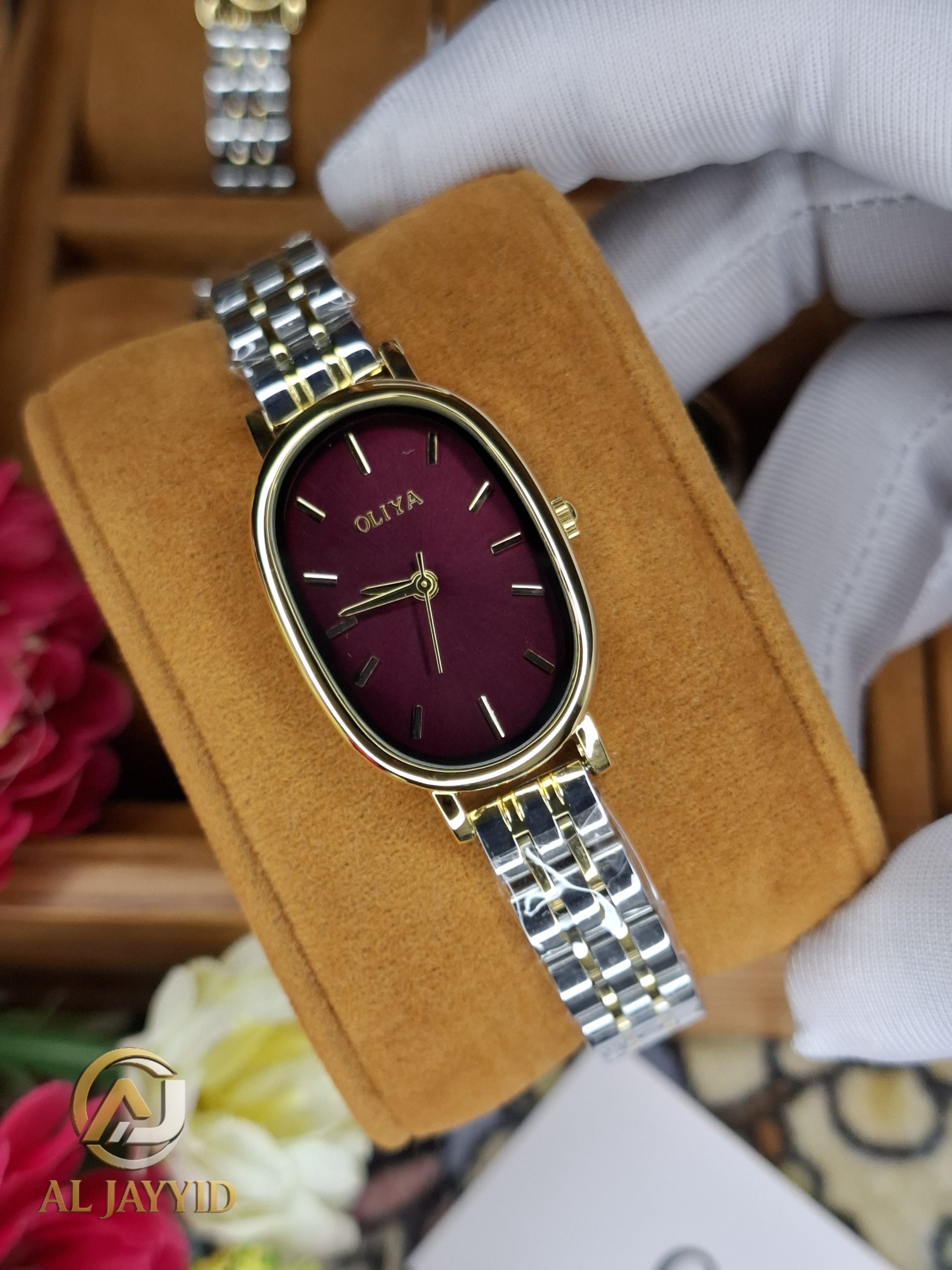 A close-up view of the OLIYA 2015 women's watch, showing its oval golden case, burgundy dial, and two-tone bracelet.
