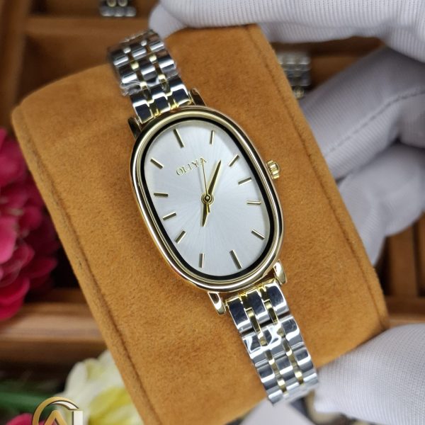 A gloved hand holding the OLIYA 2015 women's two-tone watch, showing its oval gold case and silver and gold link bracelet.