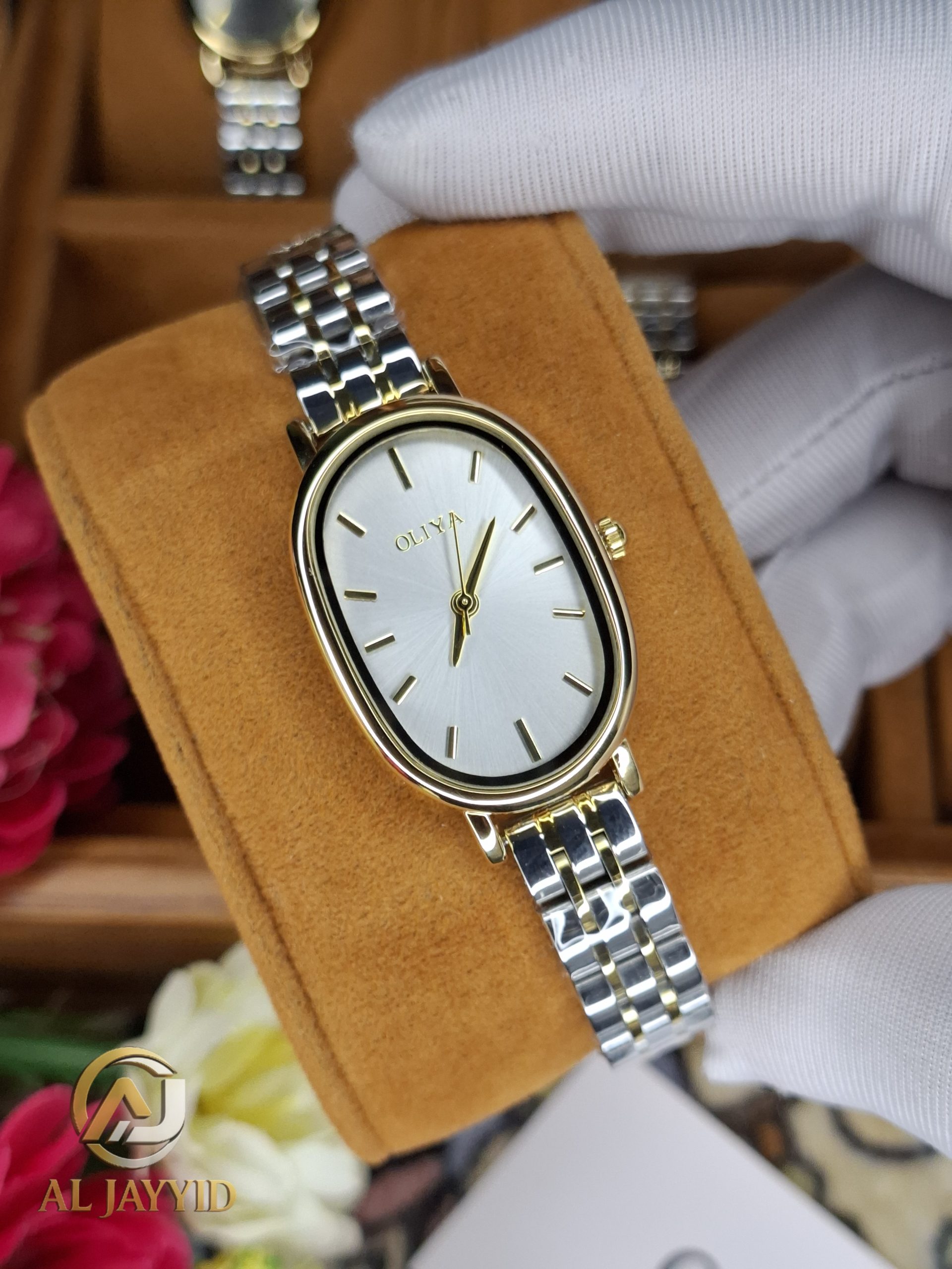A gloved hand holding the OLIYA 2015 women's two-tone watch, showing its oval gold case and silver and gold link bracelet.
