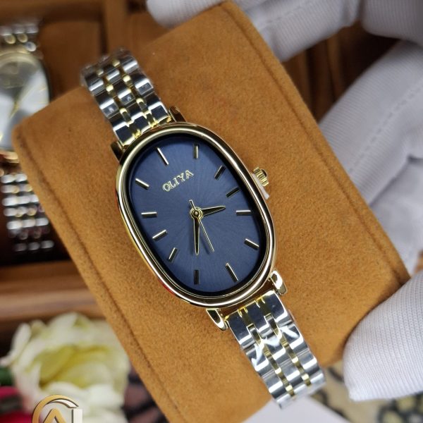 A gloved hand holding an OLIYA 2015 women's watch, featuring a blue oval dial and a two-tone gold and silver bracelet.