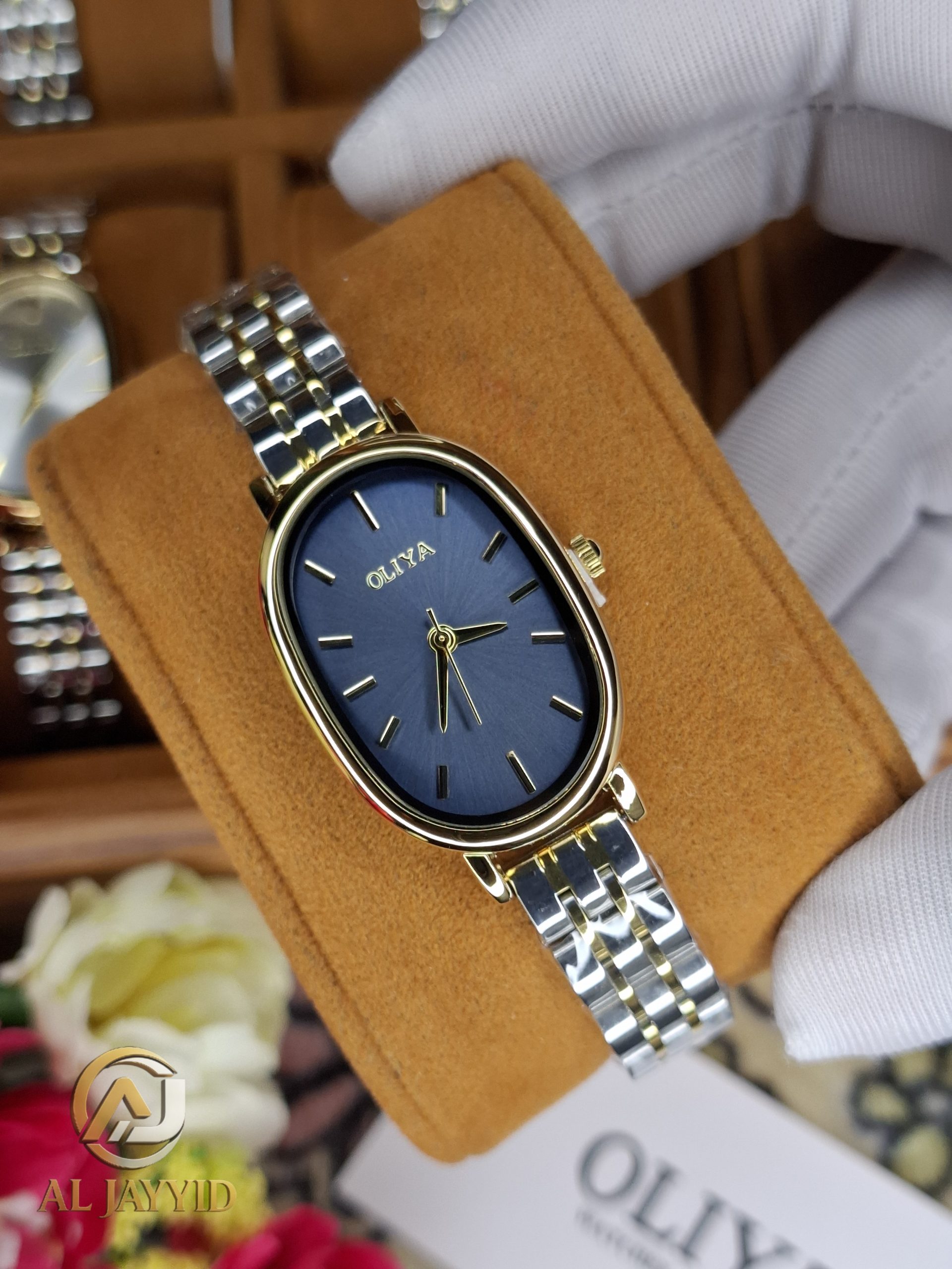 A gloved hand holding an OLIYA 2015 women's watch, featuring a blue oval dial and a two-tone gold and silver bracelet.