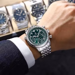 A man wearing the POEDAGAR 960 luxury chronograph watch with a striking green dial and a polished stainless steel bracelet.