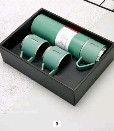 A green vacuum flask set with three matching cups neatly arranged inside a black presentation box.