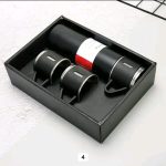 A black Vacuum Flask Set with matching cups displayed neatly inside its presentation box.