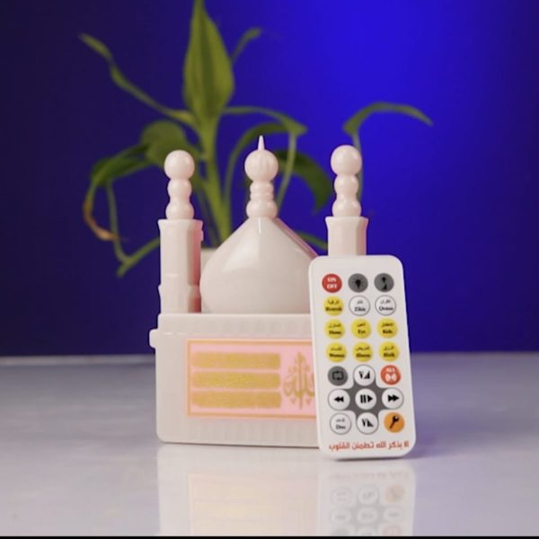 A white mosque-shaped Islamic gadget with its remote control, set against a blue background with a plant.