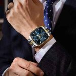 A man in a business suit adjusts his cuff, showing the POEDAGAR 866 luxury square wristwatch with a blue dial and two-tone bracelet.